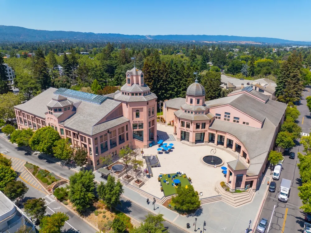 Aerial view of a large pink building surrounded by greenery and roads, showcasing its architectural design and layout.